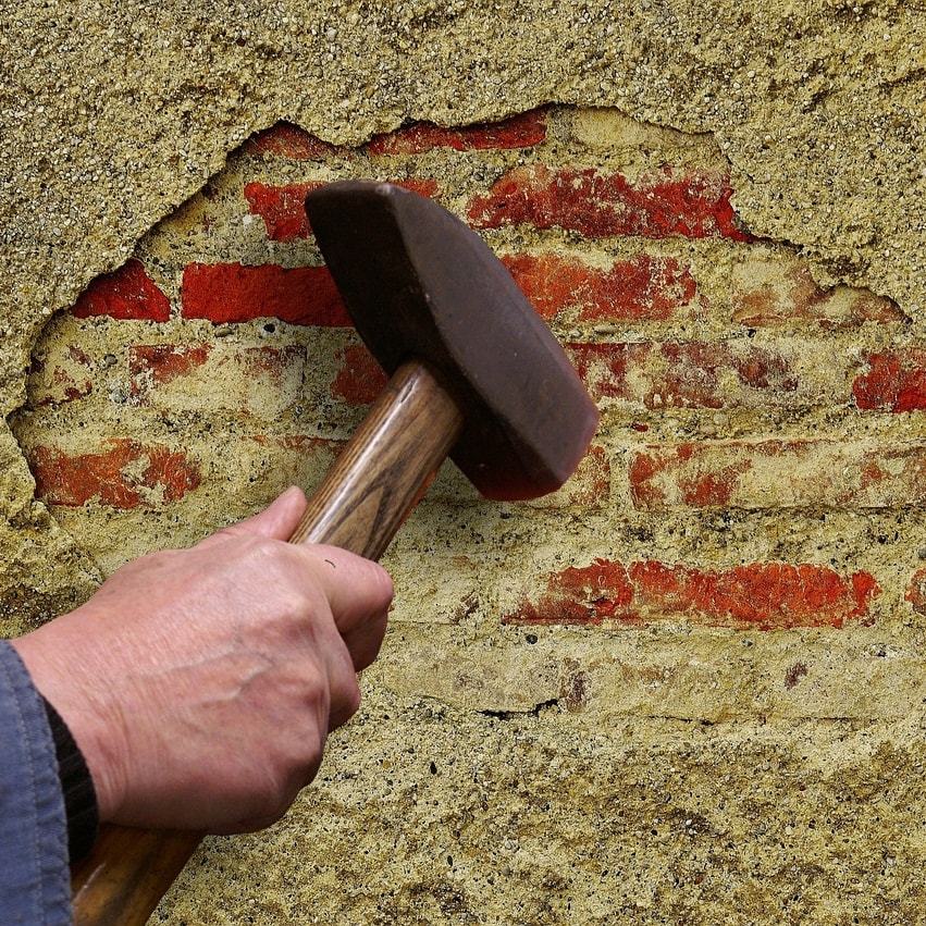 Hammer schlägt alten Putz ab, darunter kommen rote Ziegel zum Vorschein