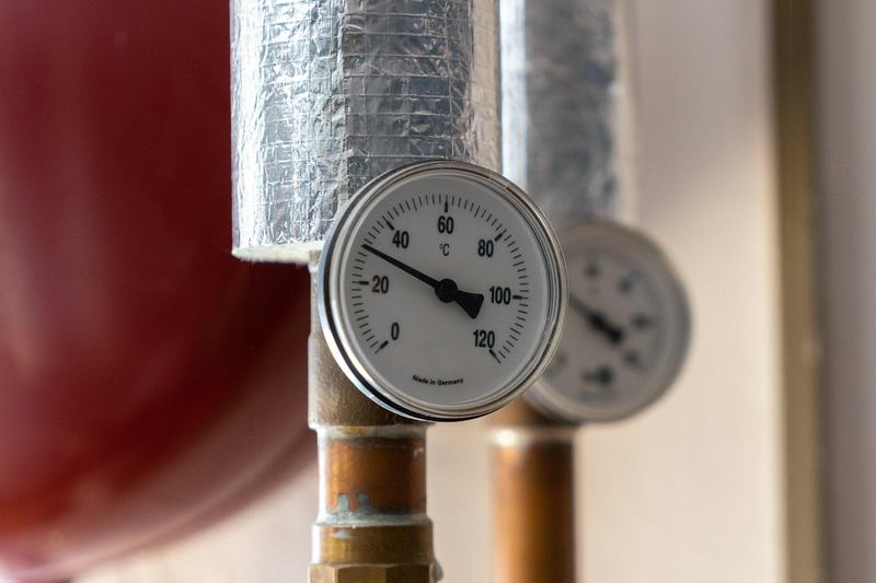 Thermometer an einem gedämmten Heizungsrohr, dahinter ein roter Speicher